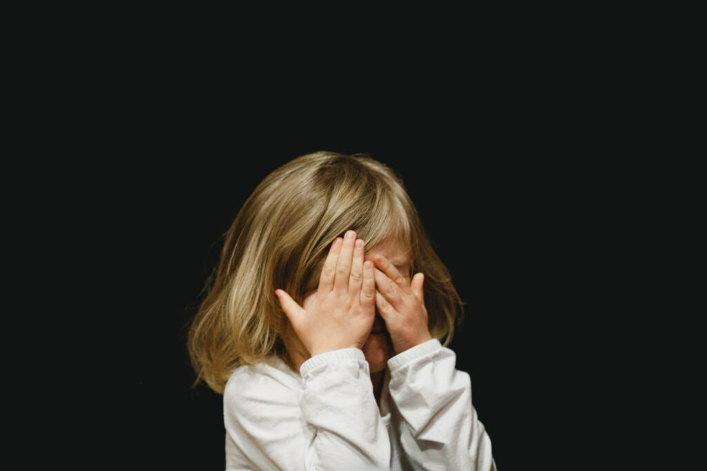 A small white child covers their face with their hands
