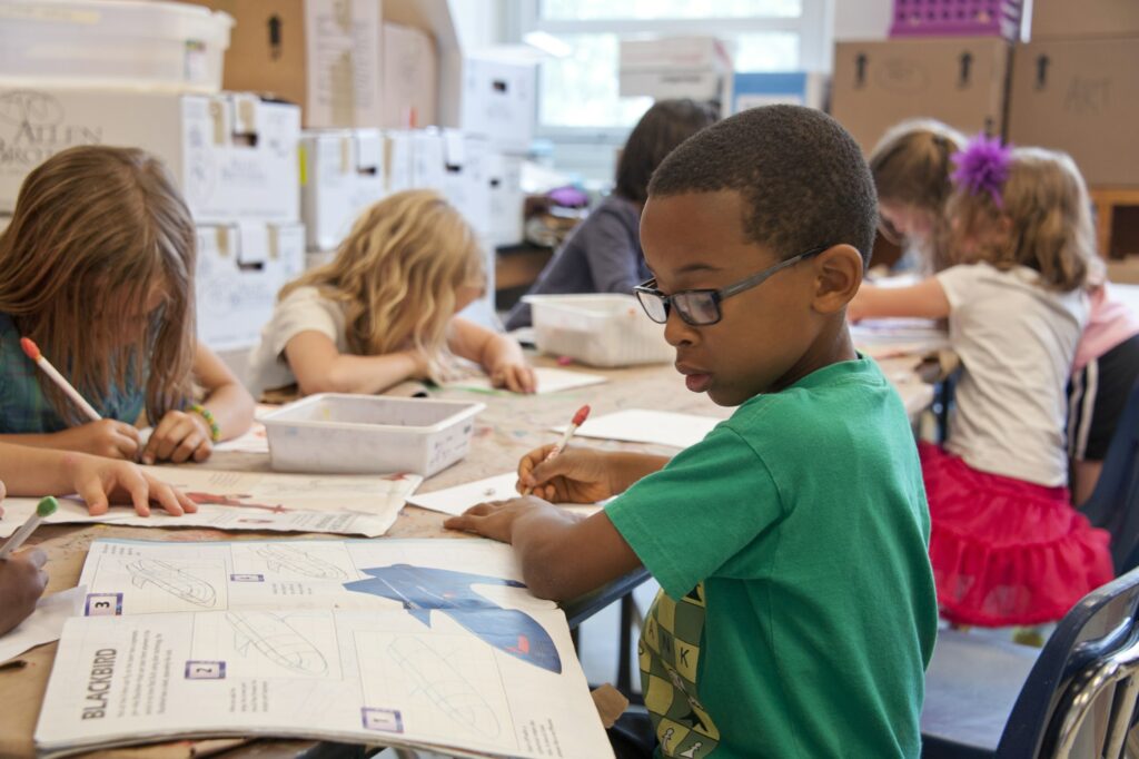 A Black boy in a green shirt in the sits in a classroom with 